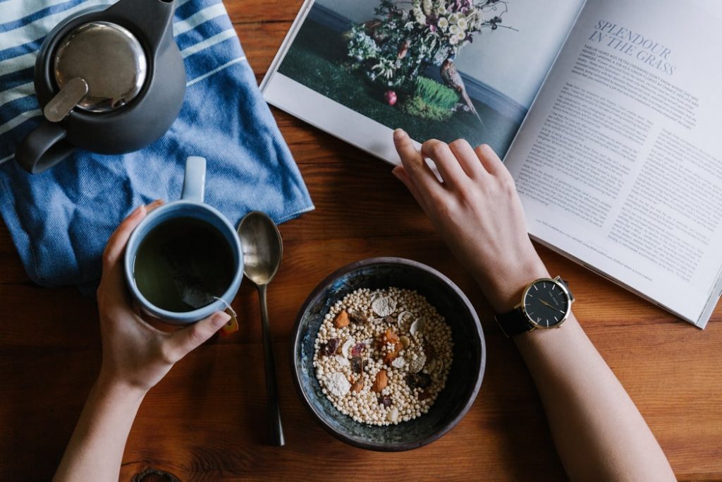 A person eating breakfast and reading a magazine 