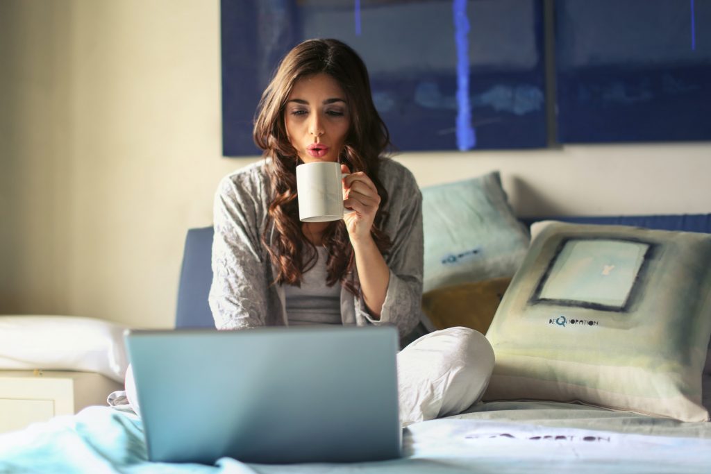woman drinking coffee remotely in front of laptop