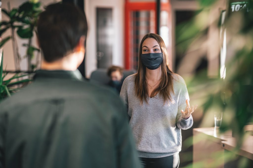 woman in face mask talking to colleague