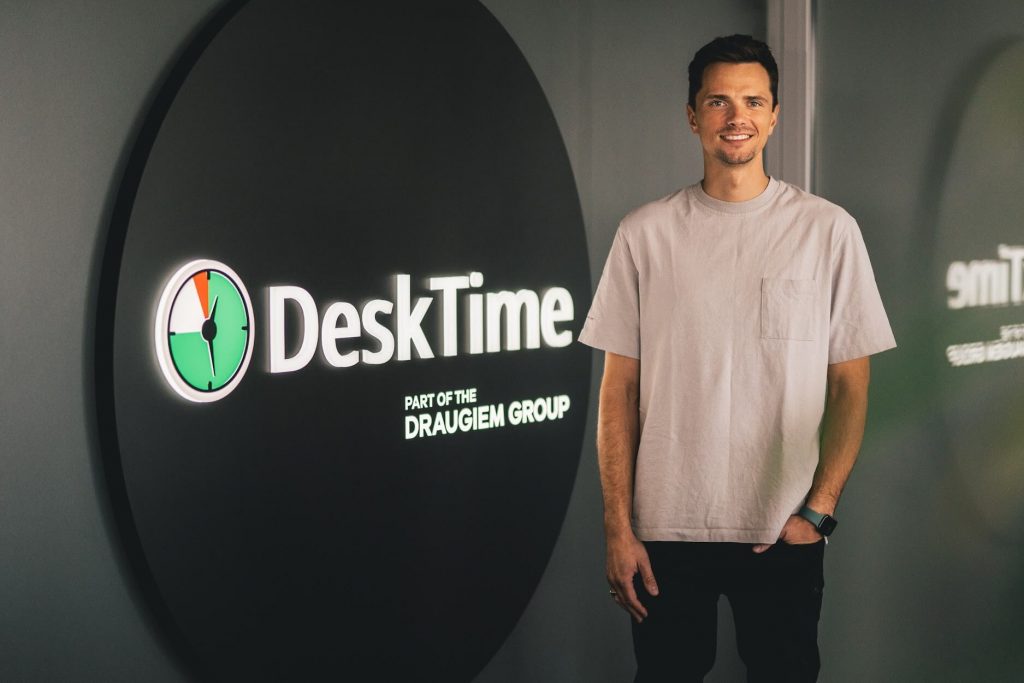 DeskTime CEO Artis Rozentals stands next to the DeskTime logo