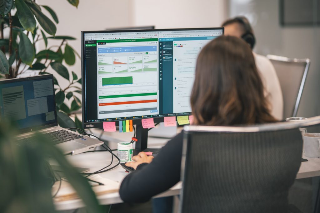 A computer monitor in an office with the DeskTime productivity  app, as well as the Slack communication tool open in a split screen, intended to depict operational efficiency 