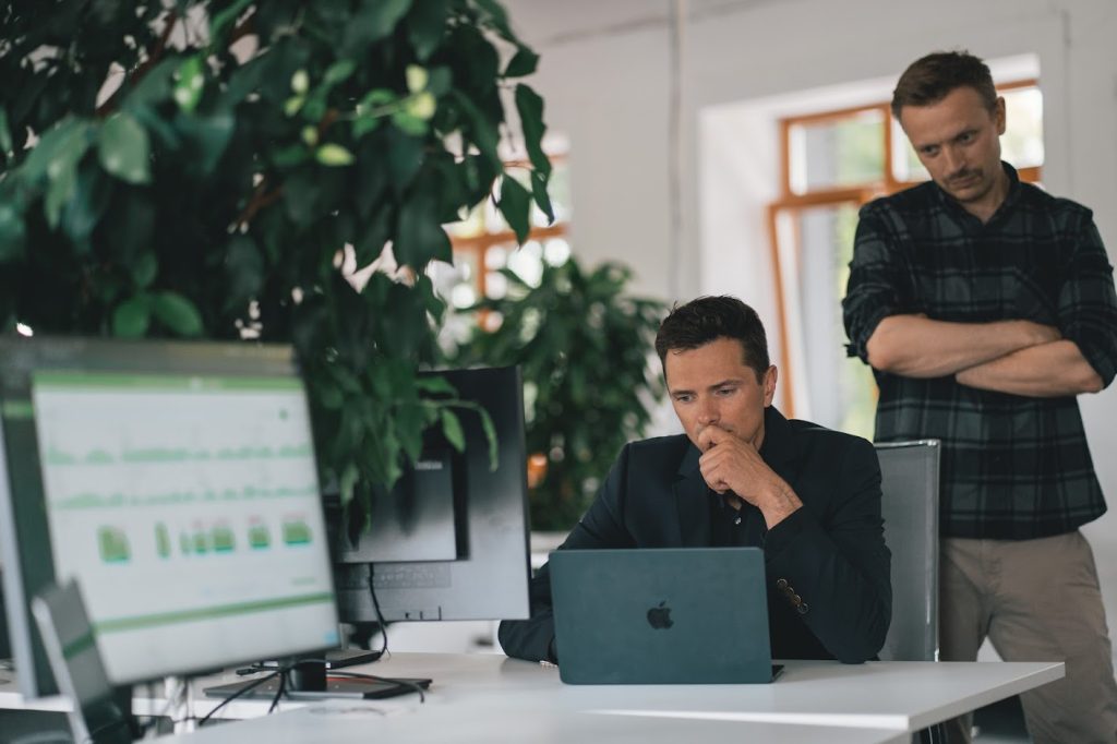 Boss manually tracking time of male employee by watching over his shoulder