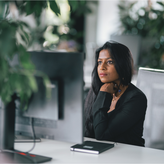 An image of a woman sitting at a desk and looking at a computer screen.