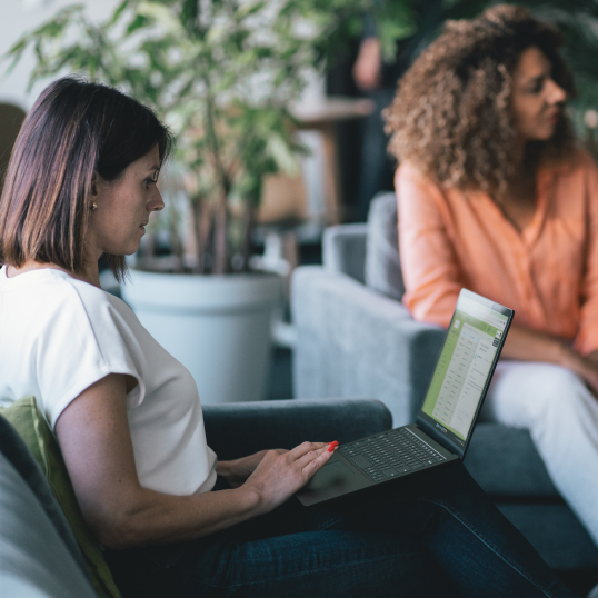 An image of a woman sitting on a couch, working on a laptop that's in her lap.