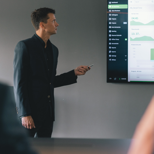 An image of a man showing a presentation on a large TV screen, holding a remote in his hands.