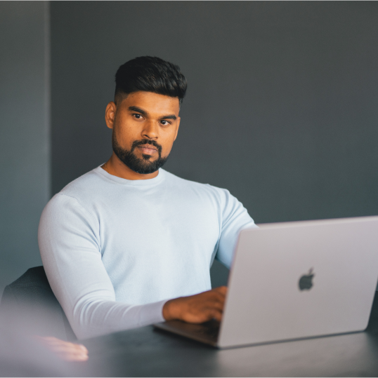 An image of a man sitting at a table with a laptop in front of him.