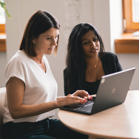 An image of two women sitting at a desk and looking at a computer.