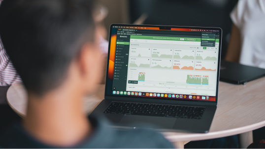 A man at a table, viewing a laptop screen that shows the DeskTime time tracker dashboard in a web browser.